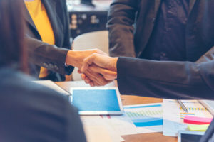 Three adults shaking hands over desk